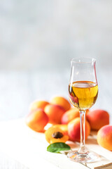 Apricot liqueur in shot glass and fresh apricots on a light wooden table.