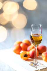 Apricot liqueur in shot glass and fresh apricots on a light wooden table in holiday colorful bokeh.