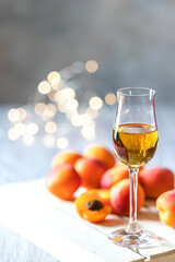 Apricot liqueur in shot glass and fresh apricots on a light wooden table in holiday colorful bokeh.