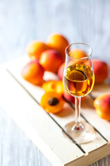 Apricot liqueur in shot glass and fresh apricots on a light wooden table.