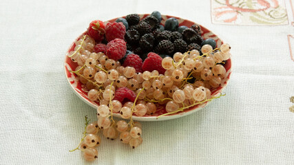 Plate with fresh blueberries, red and black raspberries, cherries and white currants.