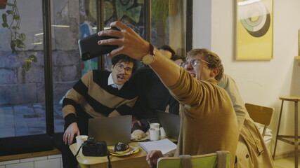 Businessmen taking selfie on smartphone. Friends making grimaces on phone camera