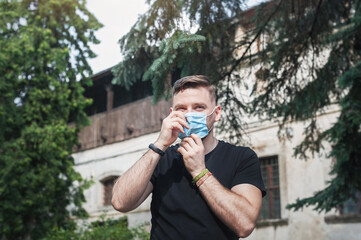 Handsome man in a disposable blue mask. Caucasian man on the street correctly puts on a face mask.