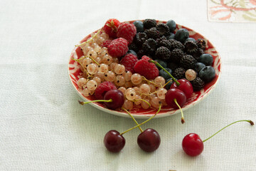 Plate with fresh blueberries, red and black raspberries, cherries and white currants.