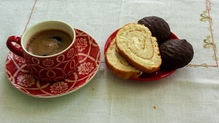 A red ceramic cup with freshly brewed coffee and a plate with a sweet dessert.