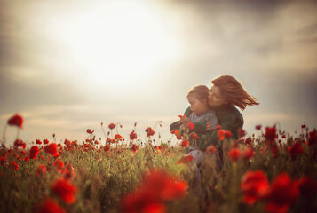 mom and daughter on a poppy field in the rays of the setting sun