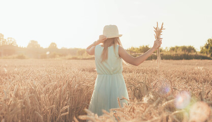 Naklejka na ściany i meble girl with spikelets of wheat and hat in a wheat field