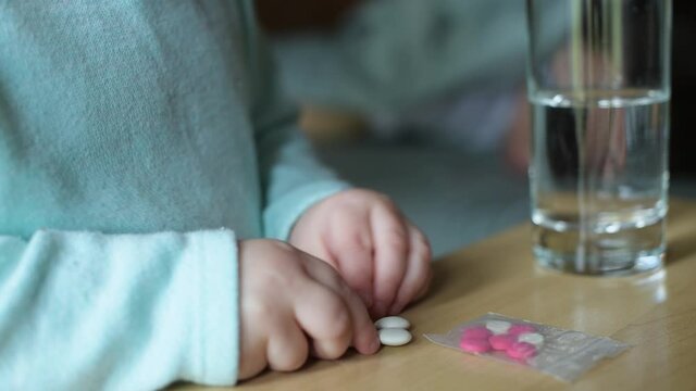 Close-up of children's hands taking pills from a bedside table near a sleeping mother