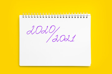 Concept of the new school year and return to school. Inscription 2020 - 2021 in a white notebook with a spiral, on a yellow background. Mockup with place for text.