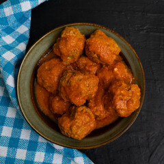 Meatballs in red sauce on dark background
