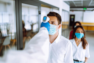 Office workers must go through fever measures using infrared digital thermometer check temperature measurement on the forehead during the coronavirus pandemic. Covid-19. 