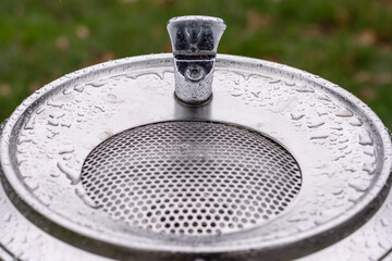 Close up of a metal drinking fountain with rain drops on the surface