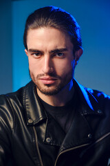 A young man of 25-30 years in in a leather jacket poses on a blue background.