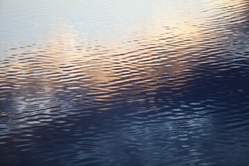 Silver surface of calm water with golden highlights and reflections. Ripples on water surface...