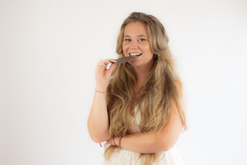 Portrait of a pretty blonde girl in a white dress eating chocolate