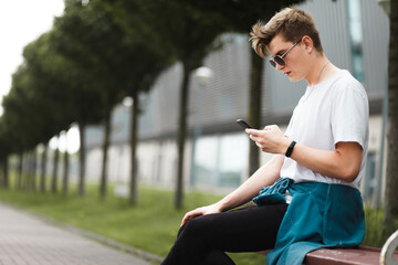 Handsome young guy sitting on a bench with a smartphone on the internet