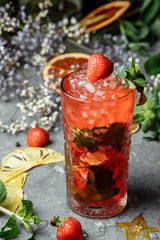 Strawberry Mojito. Cold summer mojito cocktail with strawberries, mint, lemon and ice in a glass on a table. on a dark background