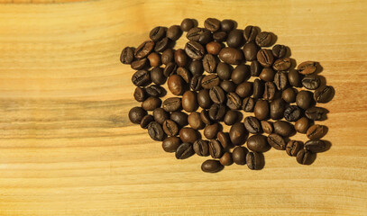 a handful of brown coffee beans on a light wooden background