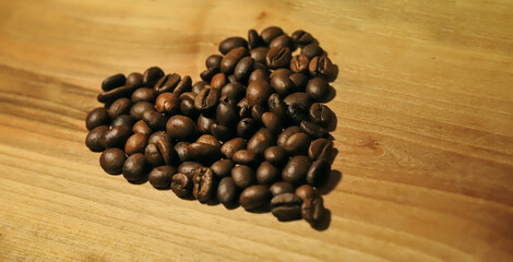 a handful of brown coffee beans in the shape of a heart on a light wooden background