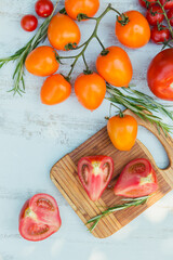 Various colorful tomatoes and rosemary herb on a light blue background