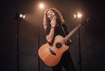 Obraz premium Middle aged hispanic man musician in black t-shirt holds guitar. View of musician in the spotlight