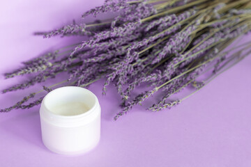 Obraz na płótnie Canvas Lavender body cream and lavender bouquet on violet background