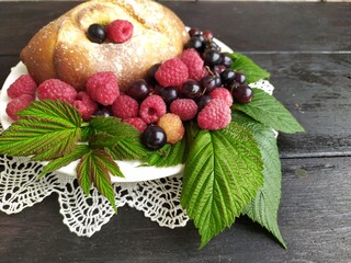 Pie with berries red ripe raspberries black currant green leaves on a white plate on a lace napkin on a black background