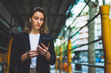 Woman listens to music with wireless headphones walking outside and hold in hand mobile phone...