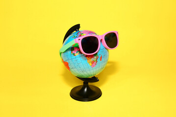 Globe in sunglasses on a yellow background. Tourism, ecology, vacation and globalism concept....