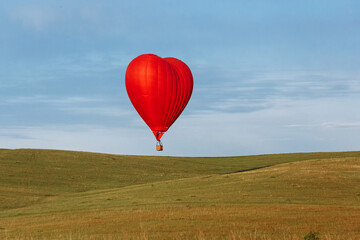 Fototapeta premium Hot air balloon in shape of heart is landing on the green field