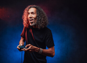 Emotional aged hispanic male with long curly hair playing video game with joystick. Hi-tech concept with vr glasses
