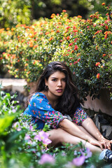 Young latina girl sitting in a garden surrounded by flowers