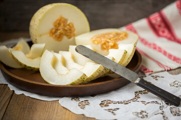 Ripe melon is cut on a dish on an old wooden table and an embroidered towel. Retro style, rustic