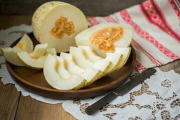Ripe melon is cut on a dish on an old wooden table and an embroidered towel. Retro style, rustic