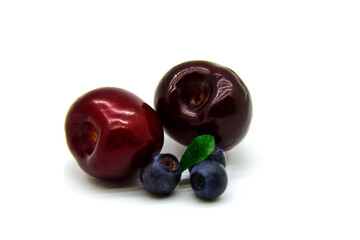 Two ripe cherries and three blueberries with a leaf