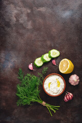 Fototapeta na wymiar Traditional greek tzatziki sauce with ingredients on dark rustic background. Greek yogurt with cucumber, dill, garlic and lemon. Top view, copy space, flat lay