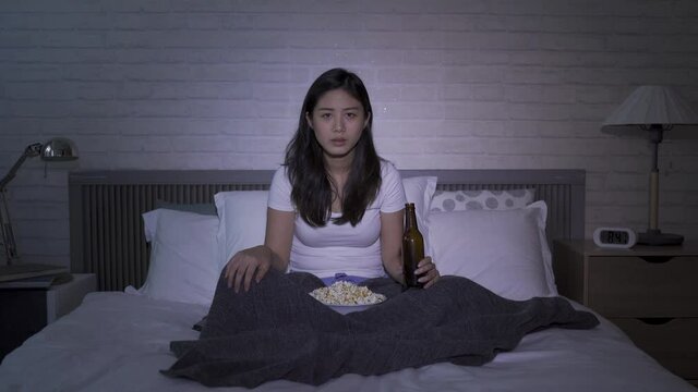 korean woman tuning to sports channel to watch live Olympic games at wee hours. girl holding beer bottle and popcorn is cheering with fist for her team at home. authentic lifestyle