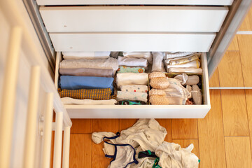 Fototapeta na wymiar Vertical storage of clothing. A pregnant girl is preparing for the birth of a child. She takes apart the clothes. Room interior. Neatly folded clothes in chest of drawers. Newborn baby clothes. 