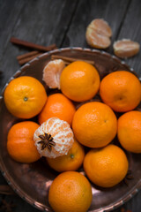 Tangerines in a copper dish on the old wooden background, table. Retro vintage style, selective focus.