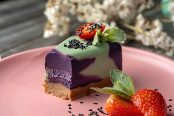 Blueberry cake, lemon, mint. Vegan, lactose free and sugar free. Laid on a pink plate, а small piece is broken off and the structure of the cake is visible.