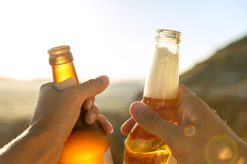 Close up cropped female and male hands holding and clanging beer glass bottles outdoor