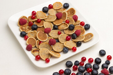 Mini pancakes and berries in plate. Red currants, blueberries  on white background.