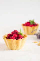 Homemade shortcrust raspberry pastry. Summer berries mini tartlets with vanilla custard and mint leaves. Fresh desserts on the white background isolated. Free copy space.
