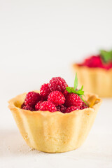 Homemade shortcrust raspberry pastry. Summer berries mini tartlets with vanilla custard and mint leaves. Fresh desserts on the white background isolated. Free copy space.