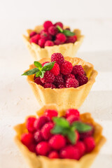 Homemade shortcrust raspberry pastry. Summer berries mini tartlets with vanilla custard and mint leaves. Fresh desserts on the white background isolated. Free copy space.
