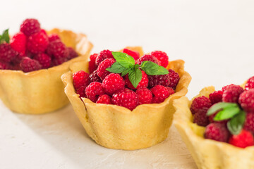 Homemade shortcrust raspberry pastry. Summer berries mini tartlets with vanilla custard and mint leaves. Fresh desserts on the white background isolated. Free copy space.