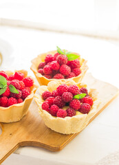 Homemade shortcrust raspberry pastry. Summer berries mini tartlets with vanilla custard and mint leaves. Fresh desserts on the white background isolated. Free copy space.