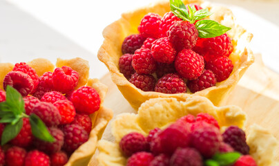 Homemade shortcrust raspberry pastry. Summer berries mini tartlets with vanilla custard and mint leaves. Fresh desserts on the white background isolated. Free copy space.