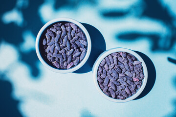 Honeysuckle berries in a blue bowl on a blue background. Shadows. Harvest