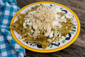 Mexican green chilaquiles with chicken and cheese on wooden background